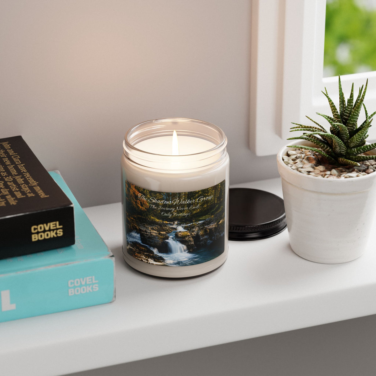 Lit Be Still soy candle with river scene label on a windowsill beside a succulent